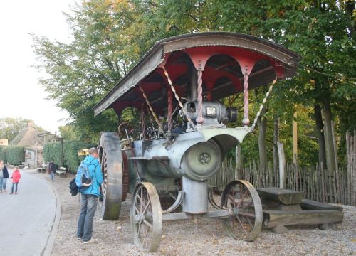 Neben dem Lokomobil steht ein Mann. Er schaut sich das Lokomobil genauer an.