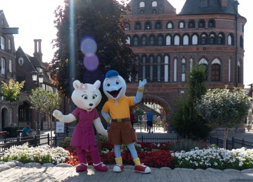 Die Maskottchen Flipsi und Emmi steht vor dem Holstentor. Sie freue sich auf das Meet and Great.