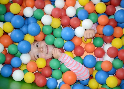 Ganz viele bunte Bälle in dem ein Kind liegt. Vom Kind sieht man Kopf und Arme.