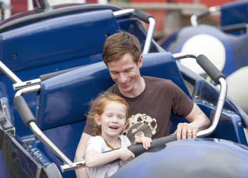 Ein Mann und ein Mädchen sitzen in der Attraktion Flying Orca. Sie sind noch nicht in der Luft.