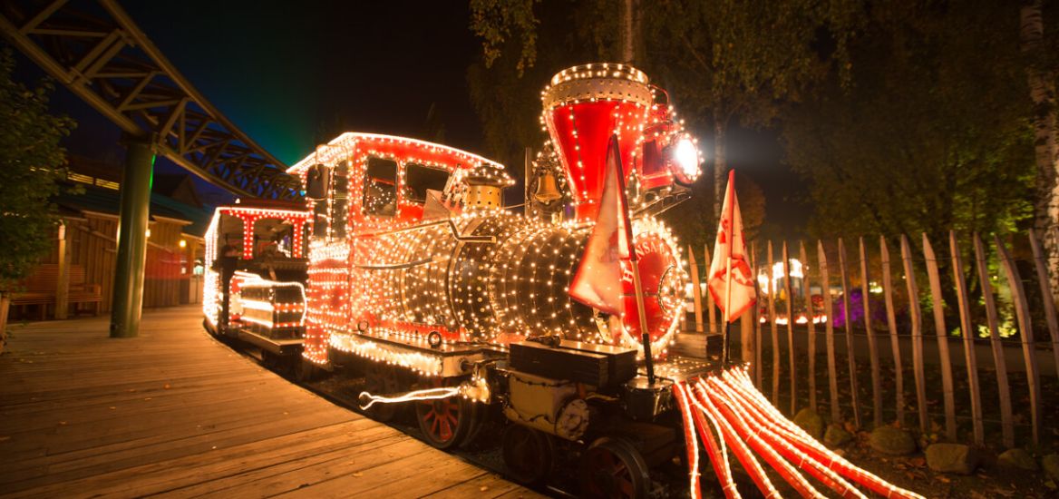 Der HANSA-PARK-Express am Bahnhof Peterhof. Der Zug wird im Dunkeln durch Lichterketten erleuchtet.