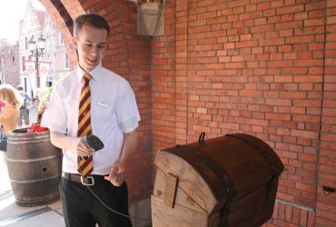 Ein junger Mann des HANSA-PARK mit einem Handscanner am Einlass scannt etwas ein. Er lächelt.