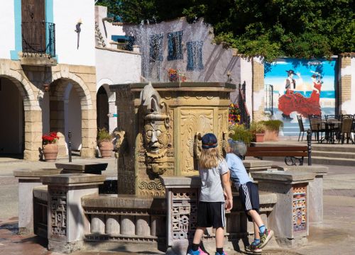 Zwei Kinder vor dem sprechenden Brunnen. Sie schauen sich den Brunnen genauer an.