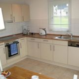 Eine Küchenzeile mit weißer Front. Mit Spülmaschine, Backofen, Herdplatte und Spüle.