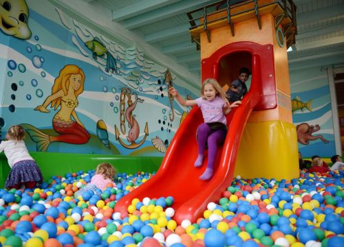 Ganz viele bunte Bälle zwischen den eine Rutsche steht. Ganz viele Kinder sind im Bällebad.