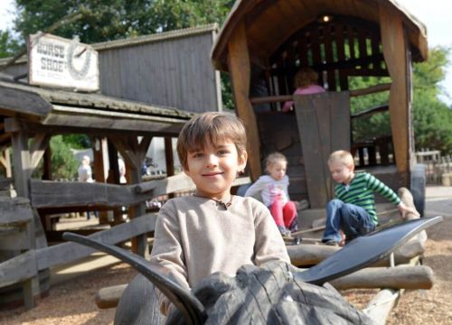 Ein Junge sitzt auf einem liegenden Pferd. Im Hintergrund klettern Kinder in der Postkutsche.