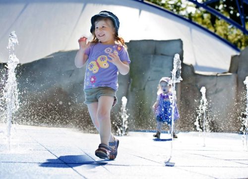 Zwei Mädchen laufen durch die kleinen sprudelnden Wasserfontänen des Wasserspielplatz Super Splash.