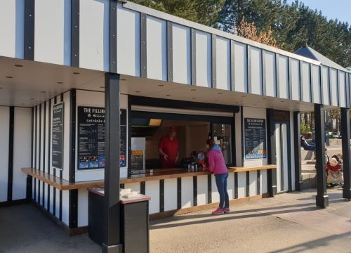 Eine Frau bestellt bei einer Servicekraft beim Kiosk Filling Station. Der Mann erklärt etwas.