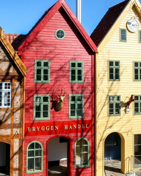 Blick auf die Arkaden des Vorplatzes. Das rote Gebäude heißt Bryggen Handel. Es hat grünen Fenster.