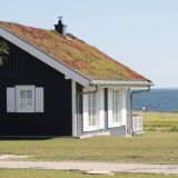 Ein Haus alleine auf dem Bild. Im Hintergrund die Ostsee. Davor ist eine längliche Rasenfläche.