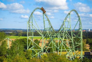 Die Schiene des Schwur des KÄRNAN erhebt sich aus den Bäumen. Im Hintergrund sind Felder.