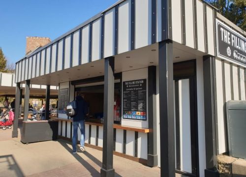 Ein Mann geht auf dem Kiosk Filling Station zu. Die Speisekarten sind links und rechts.