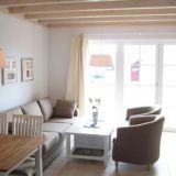 Couch mit zwei Sesseln und einen Couchtisch. Esstisch ist angedeutet. Hintergrund: Fensterfront.