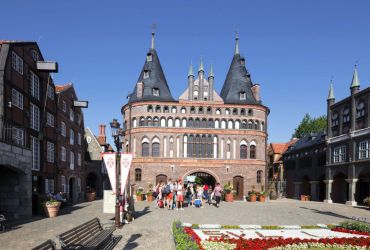Eine Gruppe von jungen Menschen steht hinter der Blumenuhr, aber vor dem Holstentor.