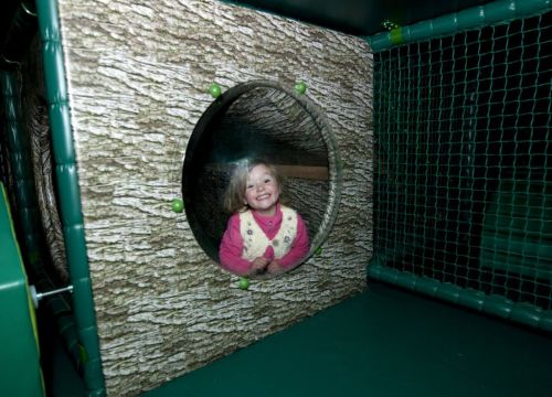 Ein Mädchen guckt aus dem runden Loch der Kletterhöhle im Tahiti Trail raus.