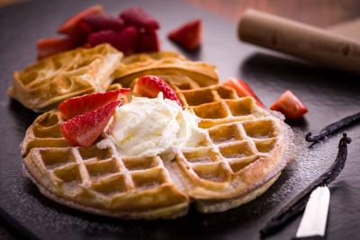 Eine Waffel auf einer Schieferplatte. Auf der Waffel sind Schlagsahne, Erdbeeren und Puderzucker.