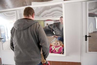 Ein Mann steht mit einem Mädchen im Kinderbuggy in der Spiegelgalerie. Sie stehen vor einem Spiegel.