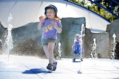 Zwei Mädchen laufen durch die kleinen sprudelnden Wasserfontänen des Wasserspielplatz Super Splash.
