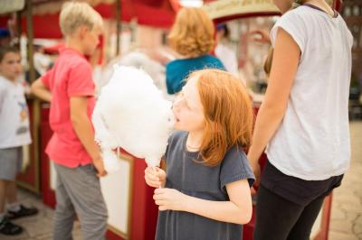 Ein Kind isst Zuckerwatte. Im Hintergrund warte andere auf Zuckerwatte.