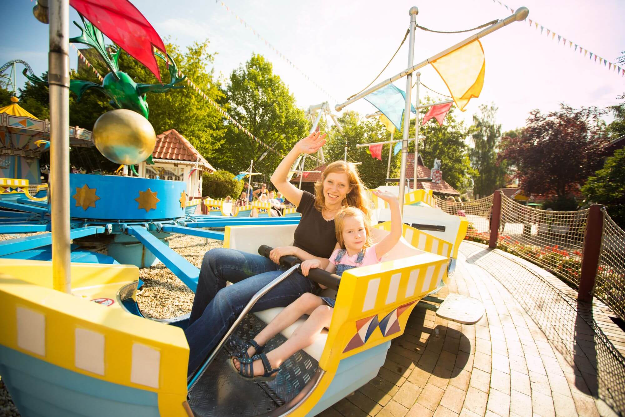 In der Attraktion Koggenfahrt winken eine Frau und ein Mädchen. Die Gondel hat einen roten Wimpel.