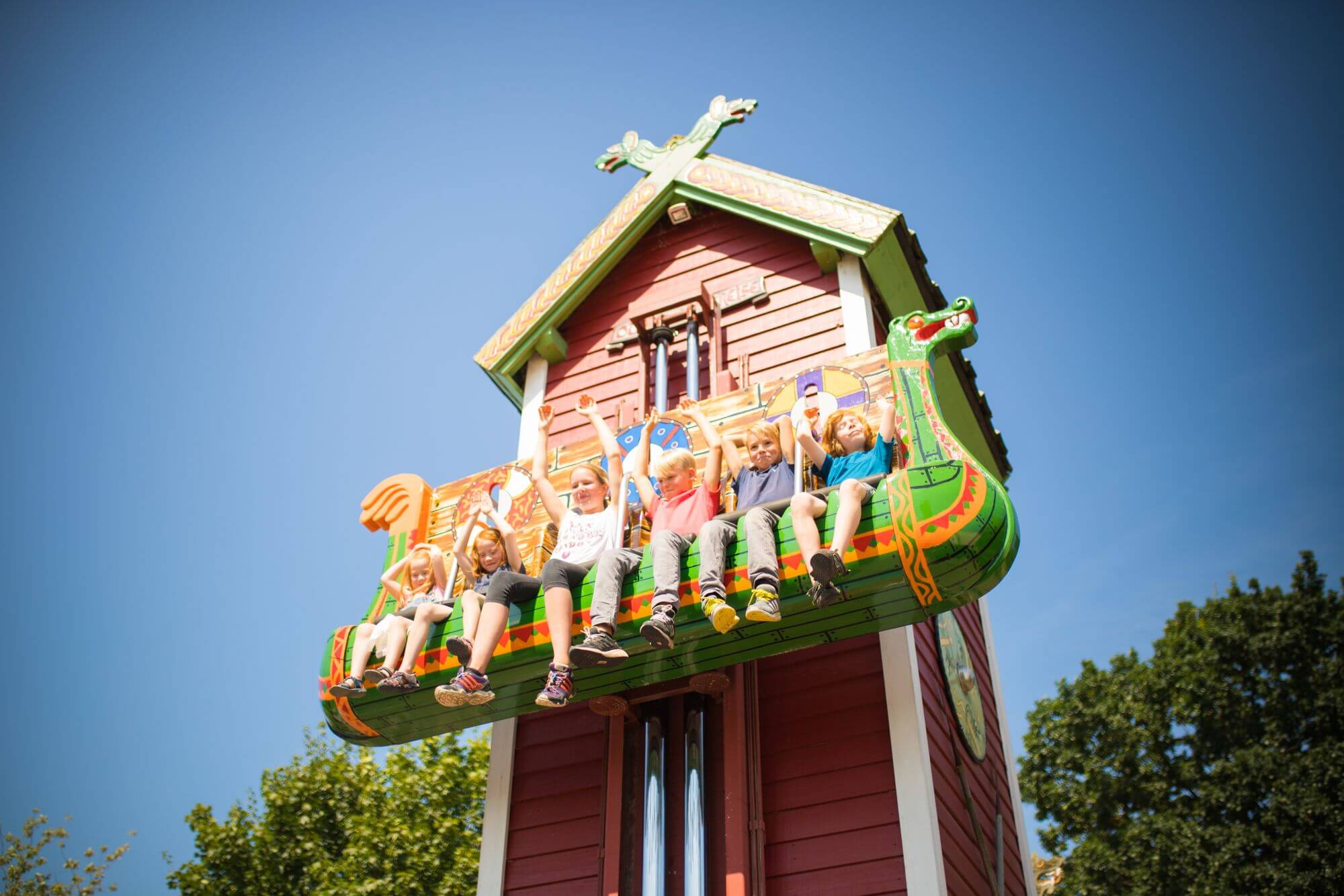 In den Sitzen von Elins Luftreise sitzen Kinder. Sie heben die Arme. Sie sind ganz oben.