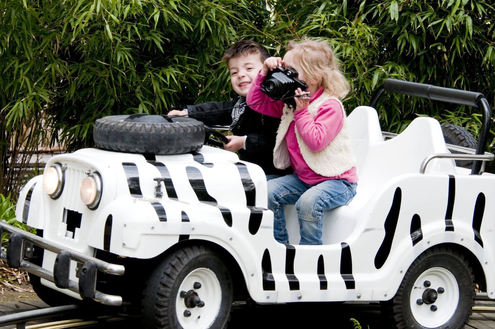 Zwei Kinder sind in einem Safari-Jeeps. Der Junge lenkt und das Mädchen hat den Fotoapparat.