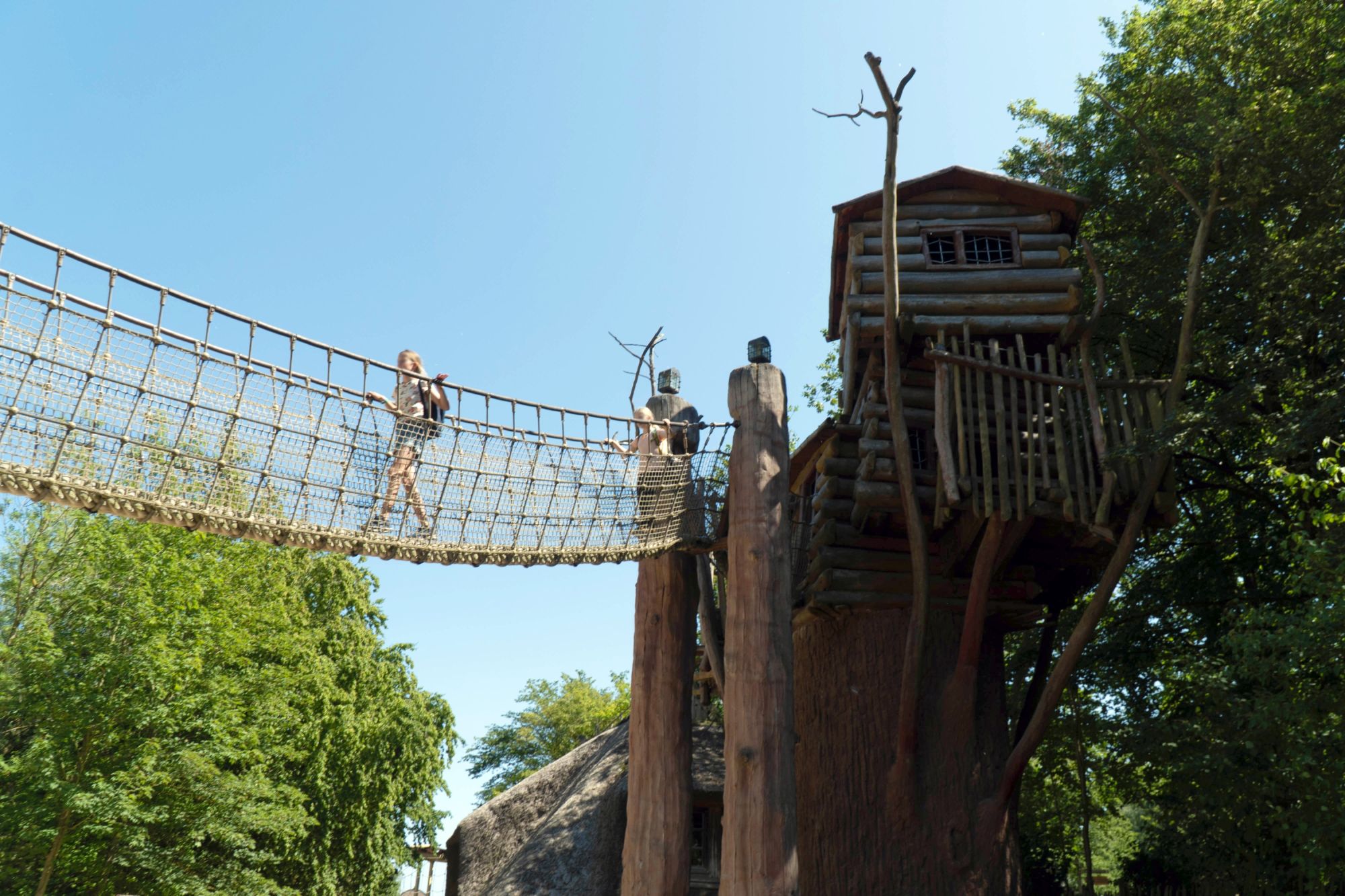 Die Apachen Lodge und Hängebrücke von unten. Zwei Mädchen laufen über die Hängebrücke.