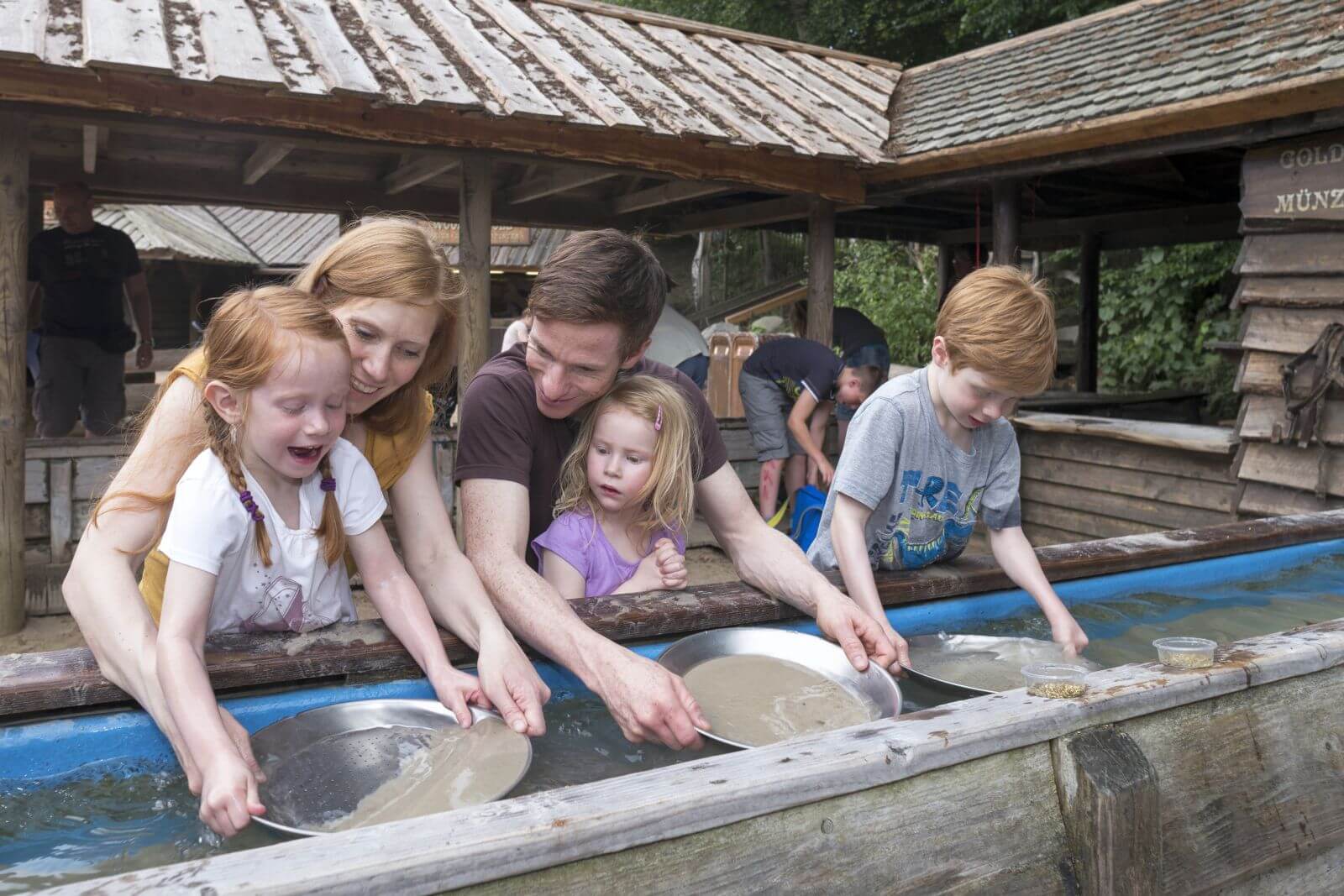 Eine Familie beim Goldwaschen. Sie habe insgesamt 3 Schalen im Wasser. In allen Schalen ist Sand.