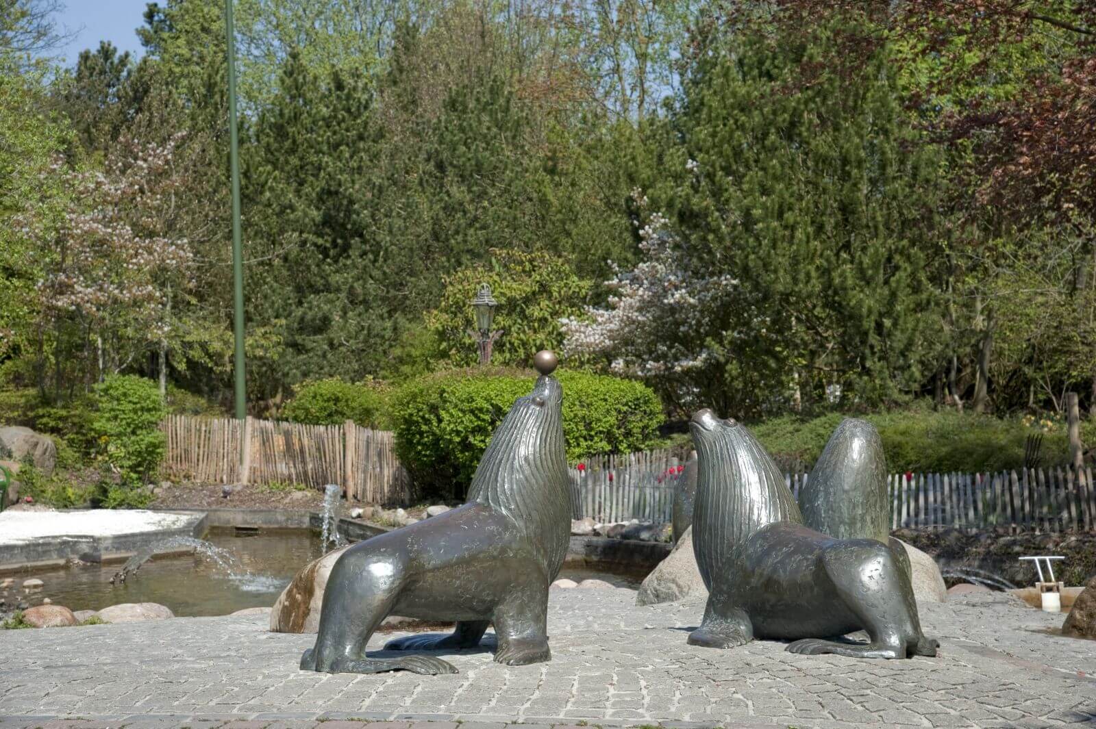 Vier Seelöwen aus Bronze vor einem Wasserspiel. Einer der Seelöwen hat einen Ball auf der Nase.