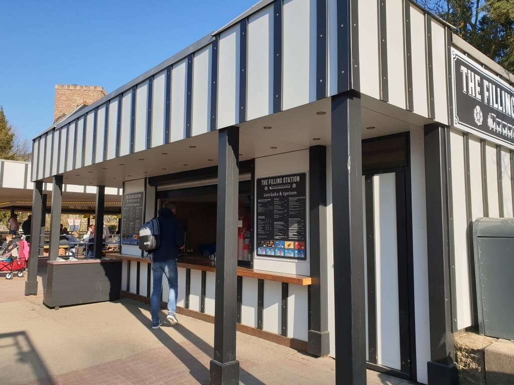 Ein Mann geht auf dem Kiosk Filling Station zu. Die Speisekarten sind links und rechts.