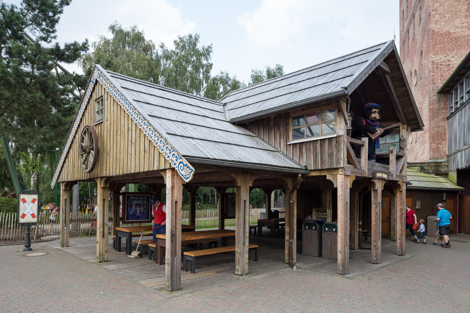 Ein Haus mit Bänken und Tischen. Ein Mann reinigt den Boden. Oben im Giebel sind muszierende Bären.