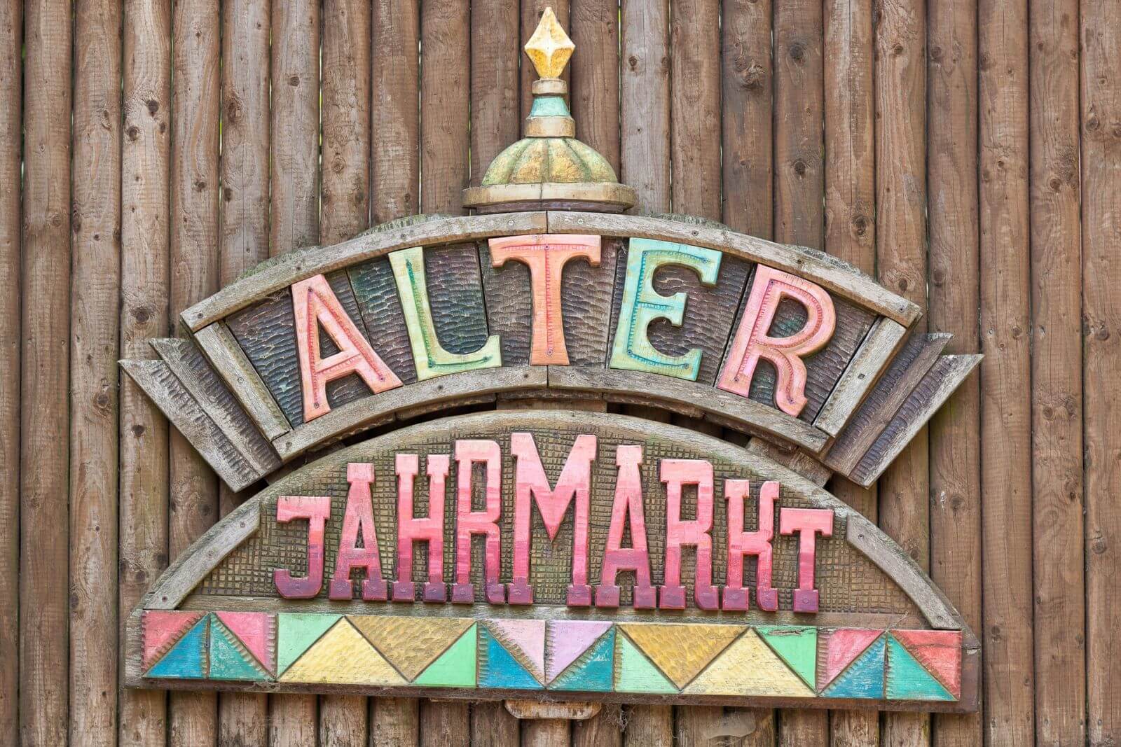 Das Schild des Alter Jahrmarkts. Es ist aus Holz. Die Deko-Elemente und die Schrift sind bunt.
