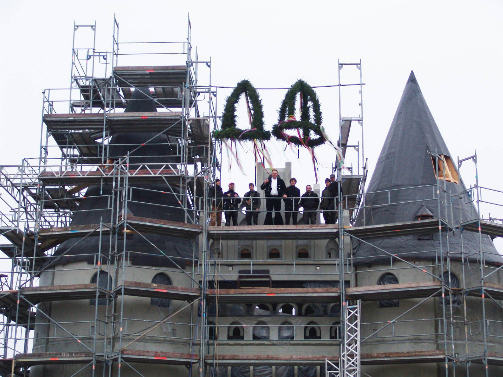 Das Holstentor in der Rohbauphase. Gerüst mit Bauarbeiter. Oben hängen zwei Richtkronen.