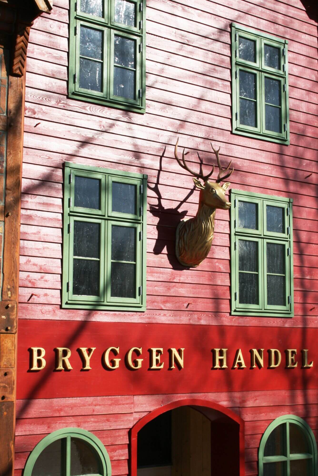 Blick auf die Arkaden des Vorplatzes. Das rote Gebäude heißt Bryggen Handel. Es hat grünen Fenster.