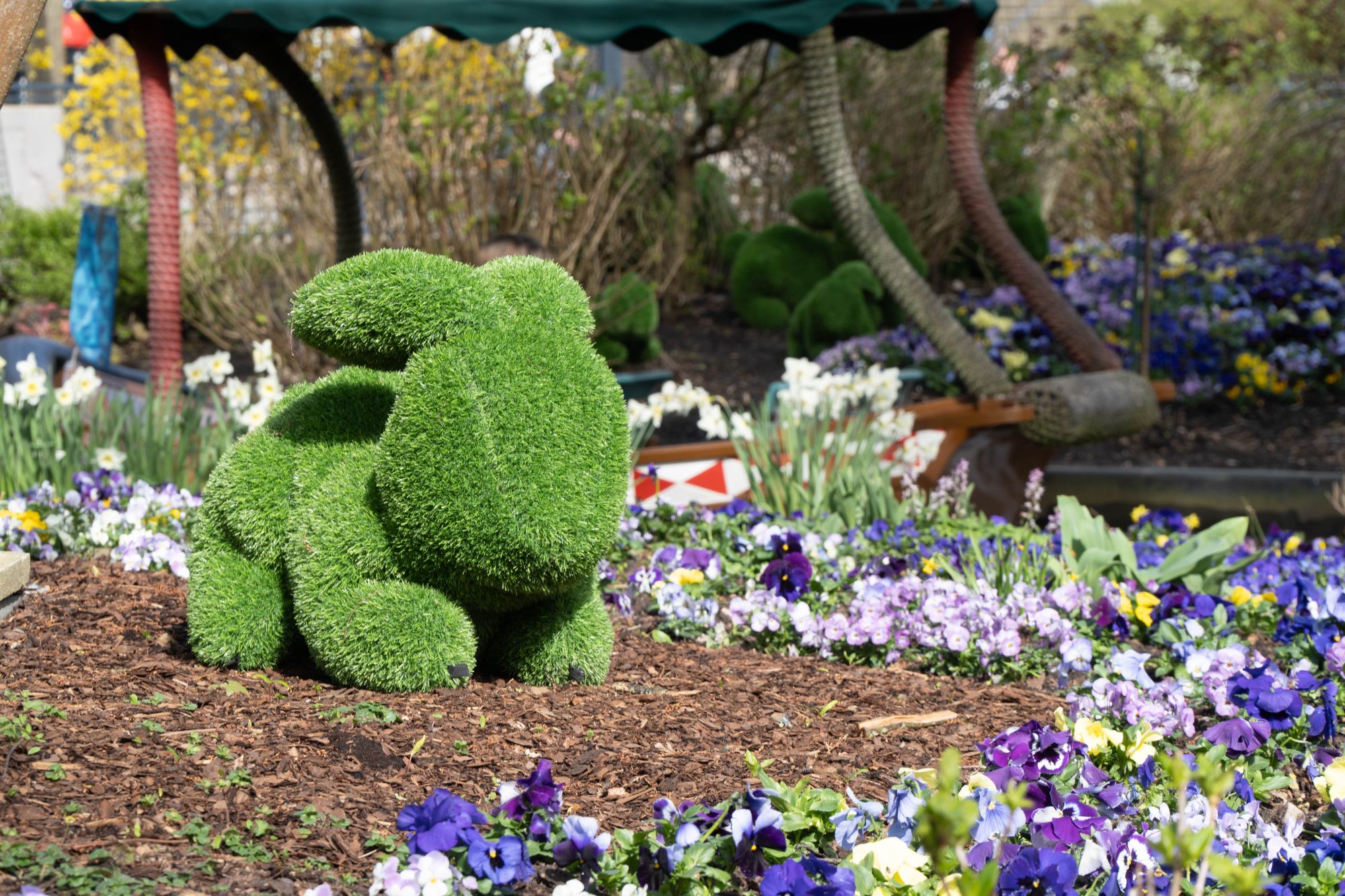 Ein grüner Rasenhase von vorne. Im Hintergrund fährt ein Boot der Blumenmeerbootsfahrt vorbei.