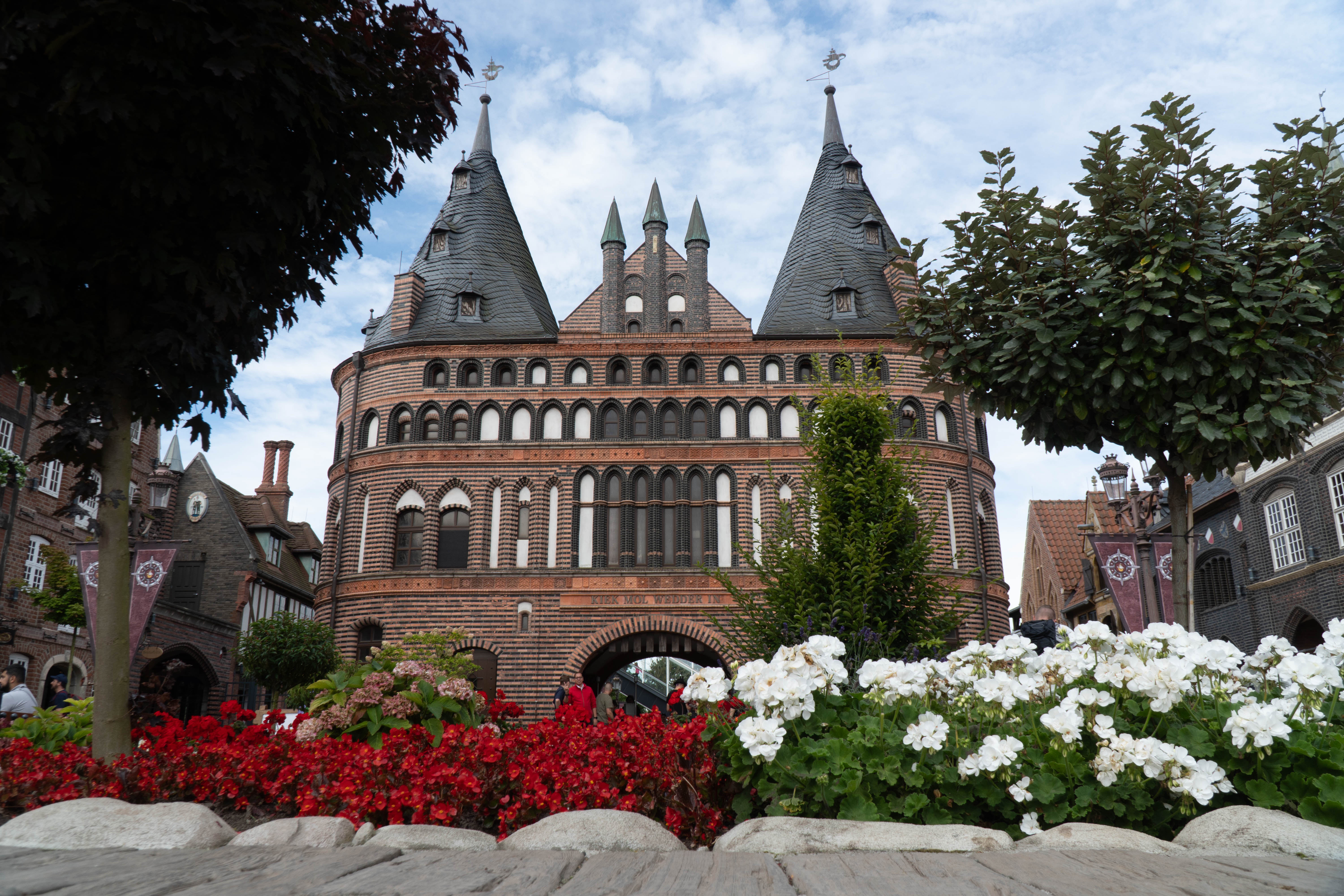 Das Holstentor von unten. Davor befinden sich Blumen und Sträucher.
