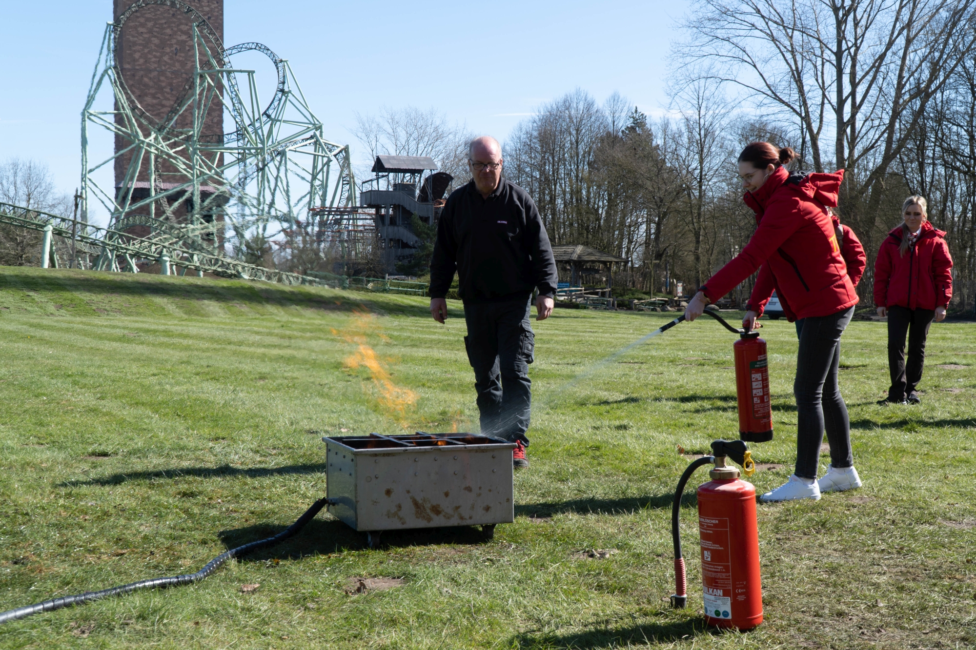 Eine junge Frau löscht mit einem Feuerlöscher ein simuliertes Feuer. Sie lächelt dabei.