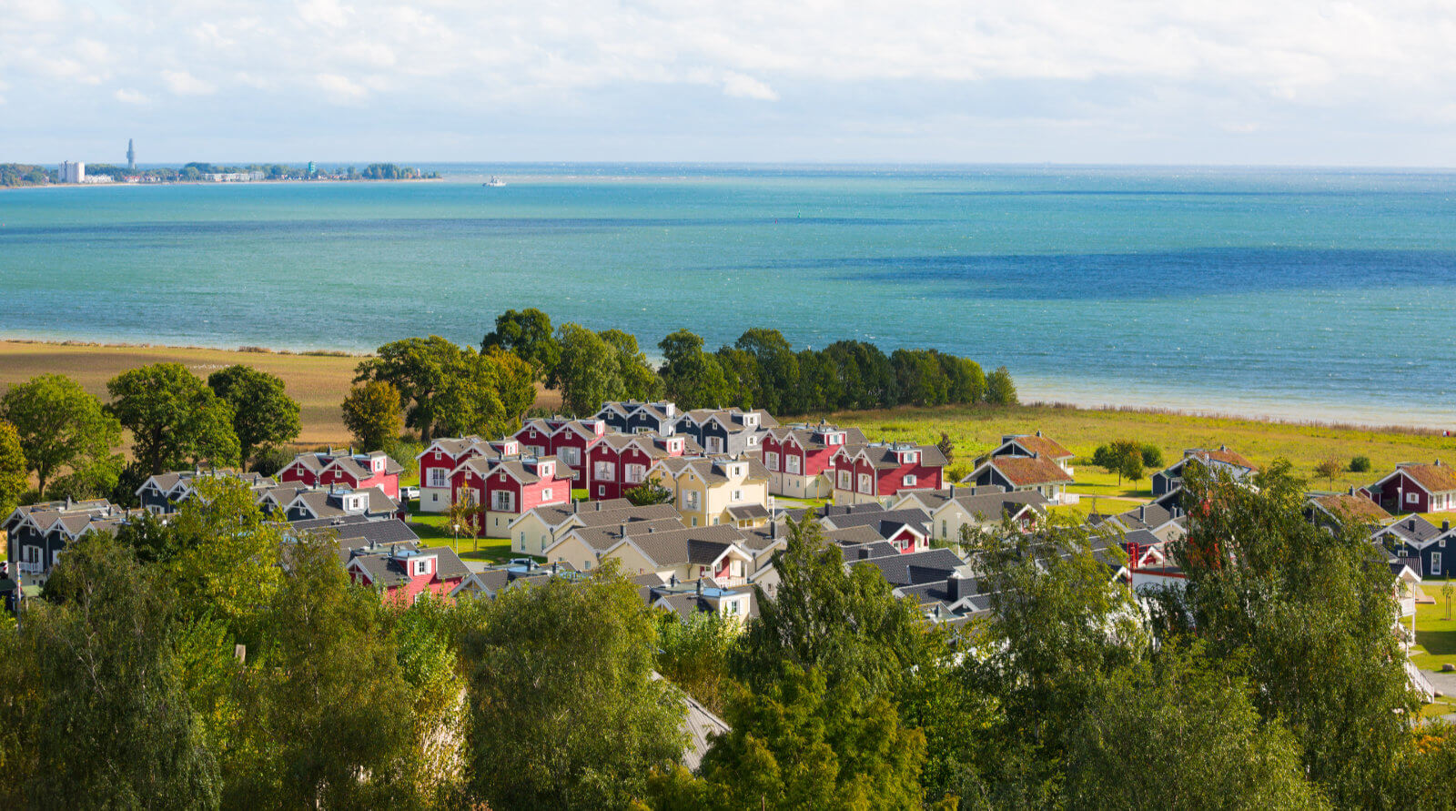 Aufnahme von oben. Die Häuser des Resorts umringt von Bäumen. Dahinter die Ostsee.